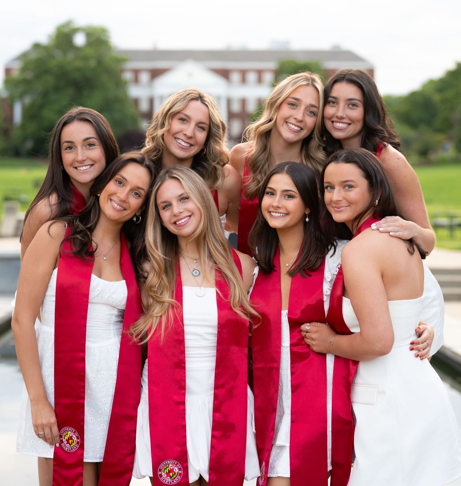 Graduates in red and white stoles posing together outdoors.