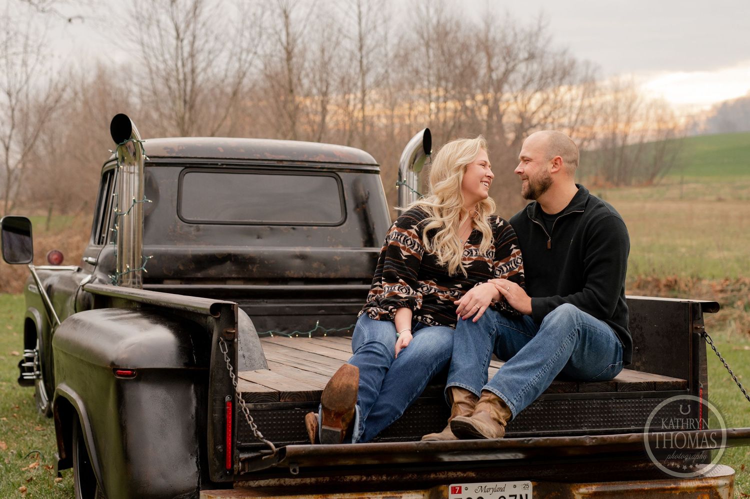 A couple shares a romantic moment while sitting in the bed of an old pickup truck during sunset.