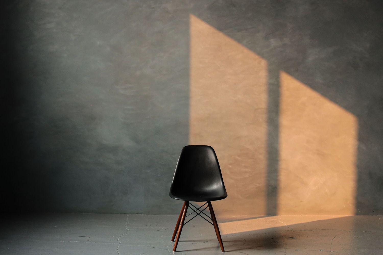Modern black Eames-style chair casting dramatic shadows on a concrete wall.