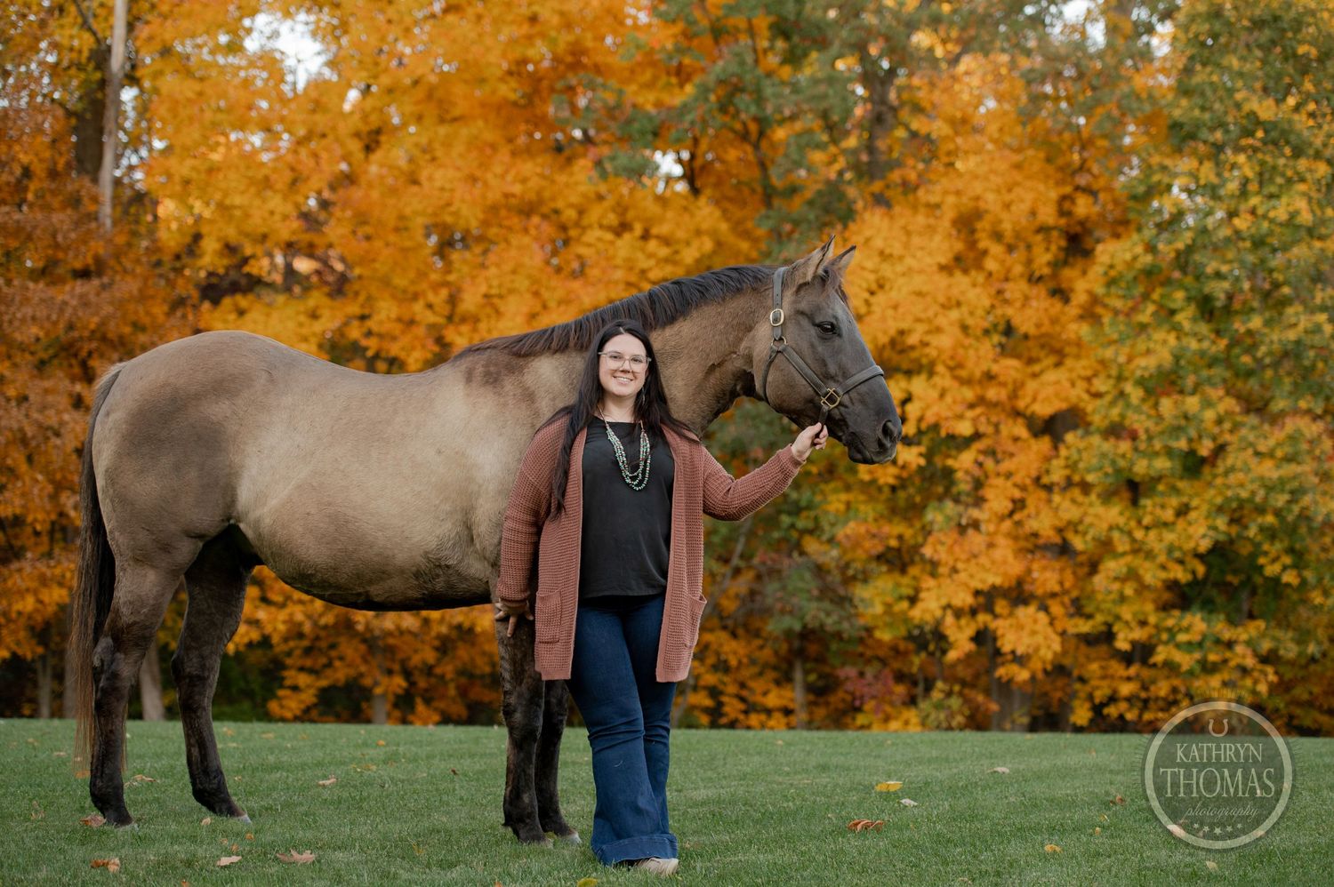 A gray horse and person pose together for a portrait with vibrant fall colors in the background.