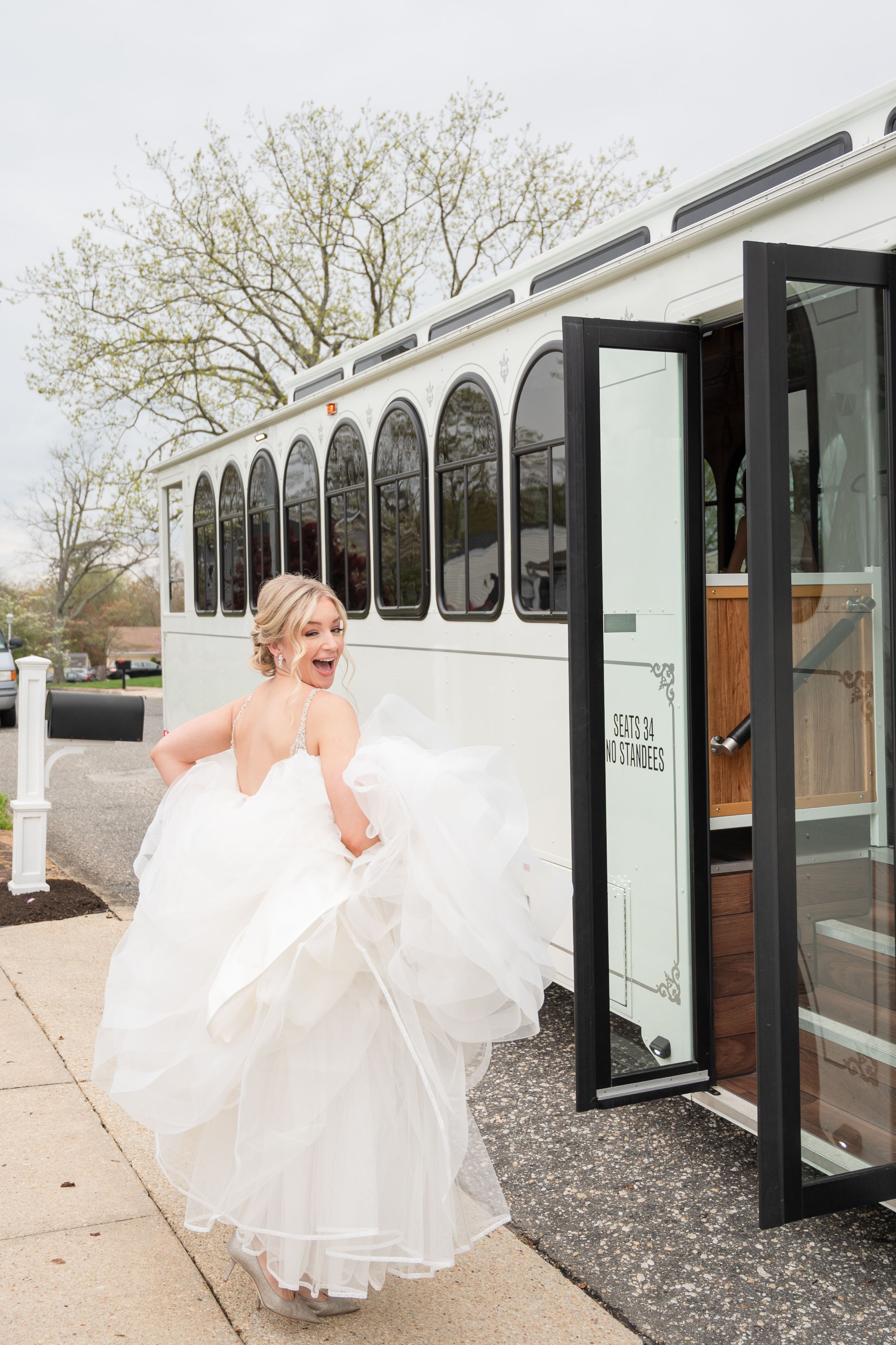 A bride in a flowing white dress walks alongside a white wedding trolley bus.