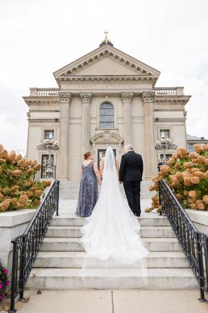 Wedding couple poses on stone steps of an elegant white classical building with ornate architecture.