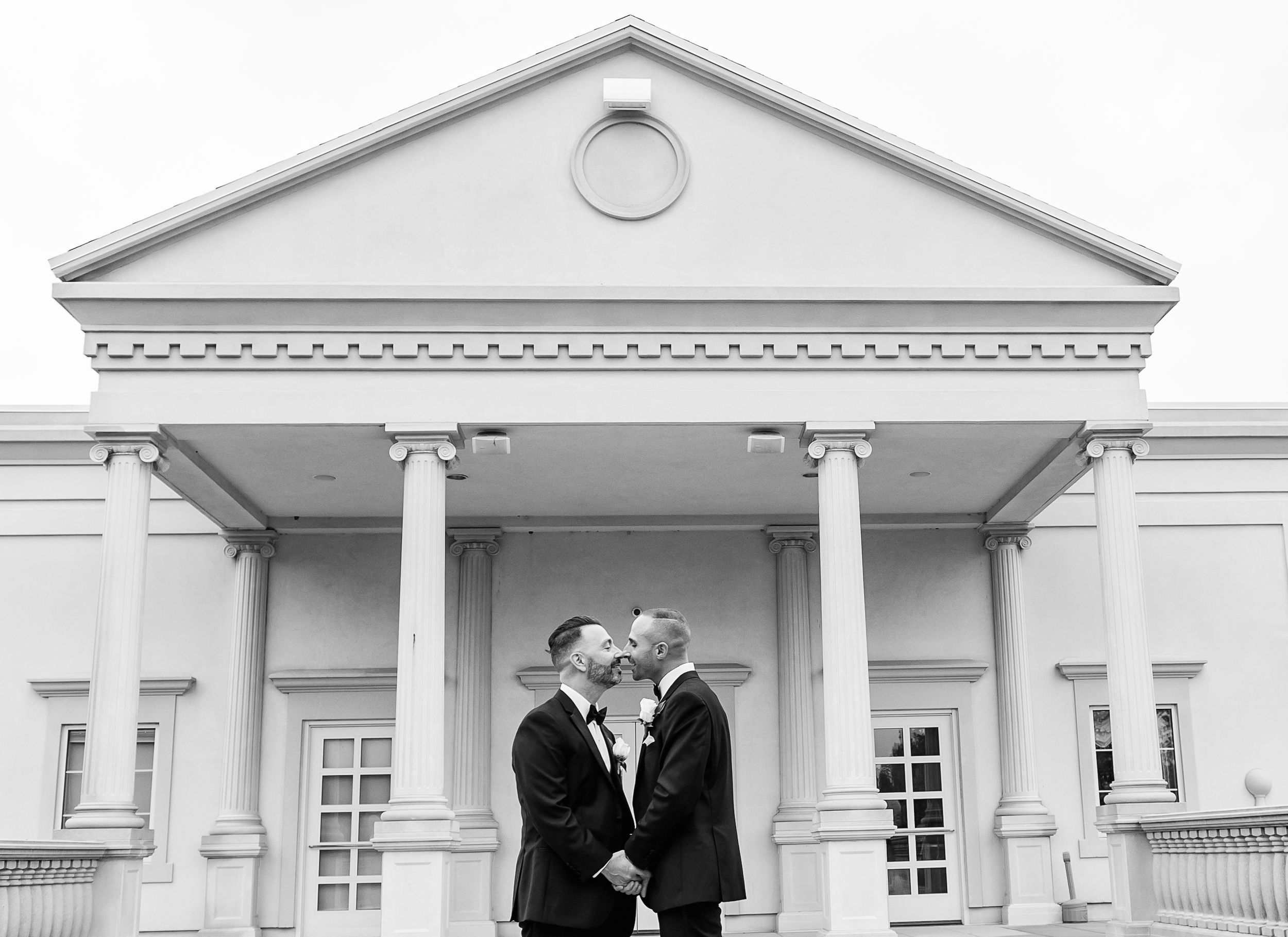 Wedding couple shares intimate moments in front of a white colonial style building with columns.