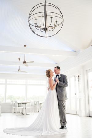 Wedding couple embraces in bright white room with modern circular light fixtures.