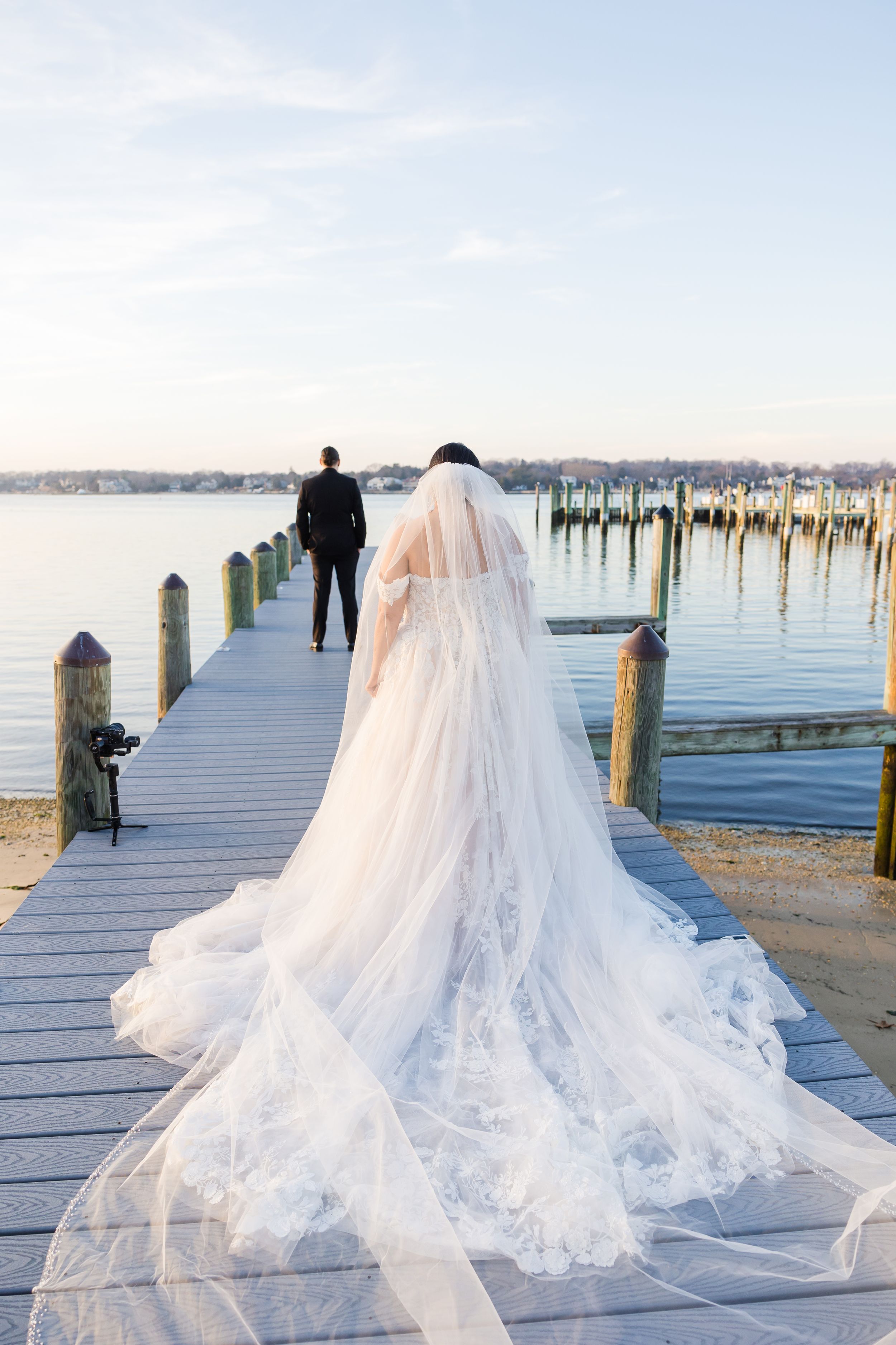 Long flowing wedding dress train on a wooden dock by the water.