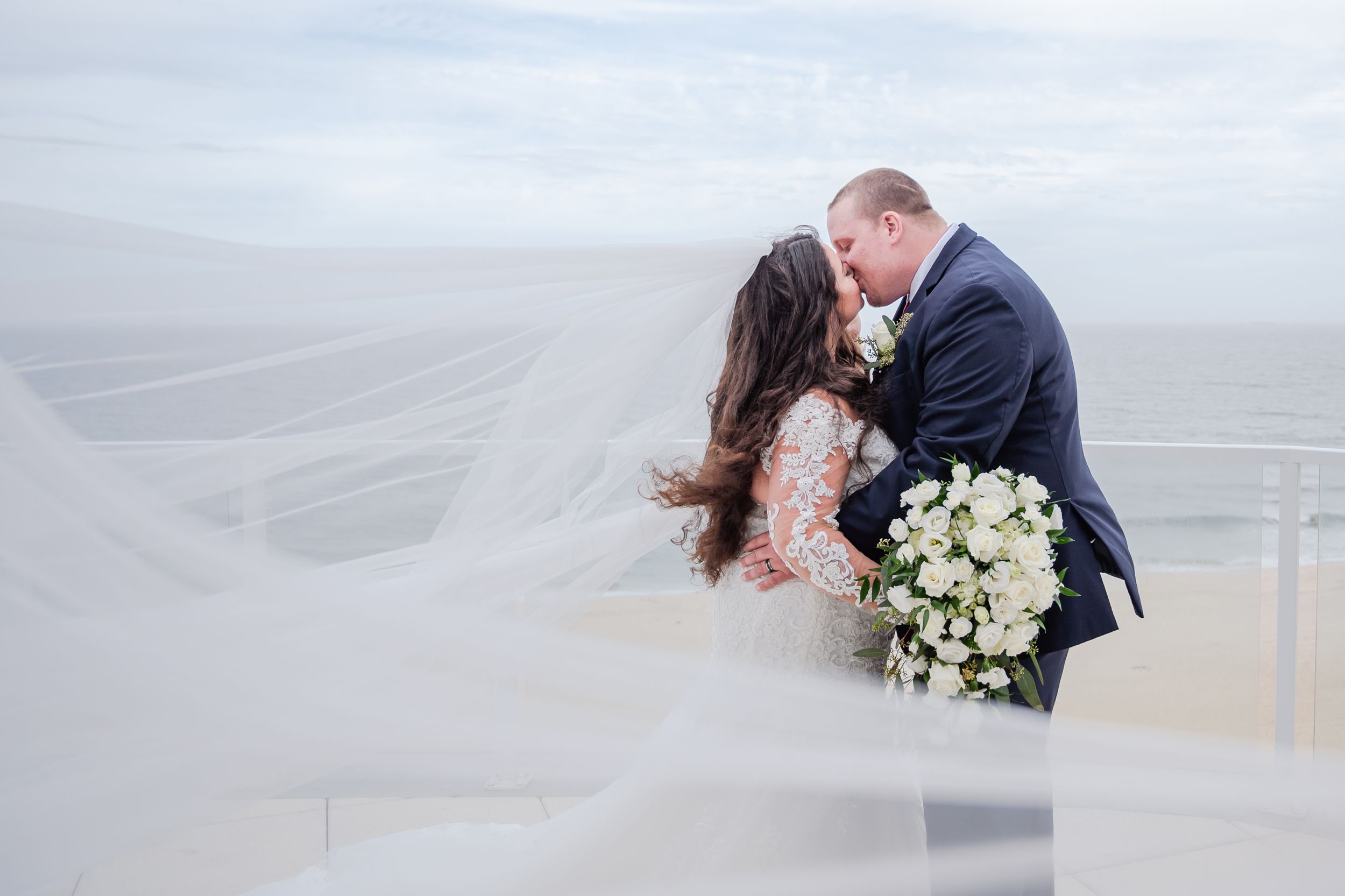 Romantic beach wedding portraits with flowing white dress and bouquet at sunset.