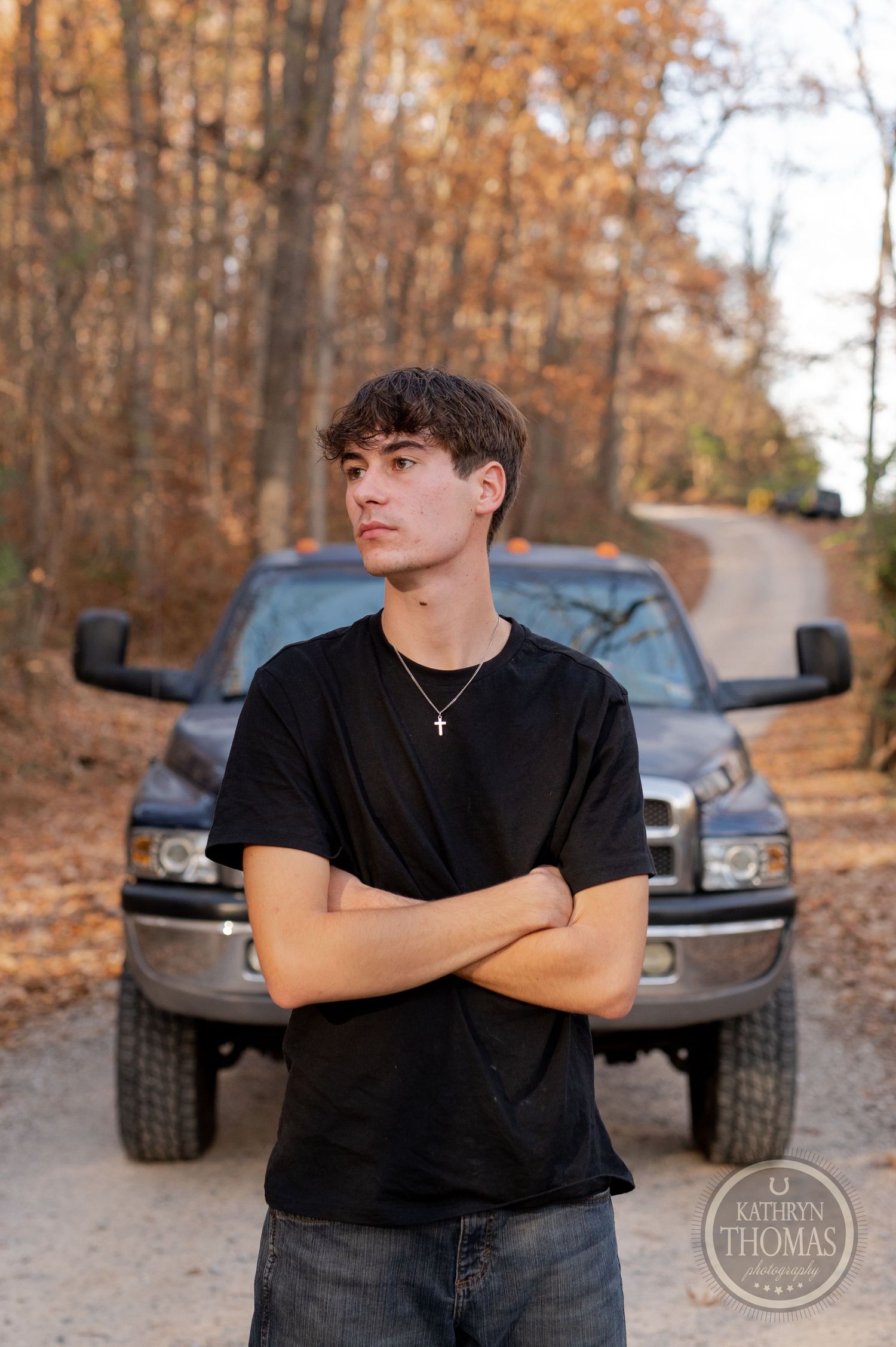 Portrait shot against silver Dodge pickup truck with autumn trees lining dirt road.