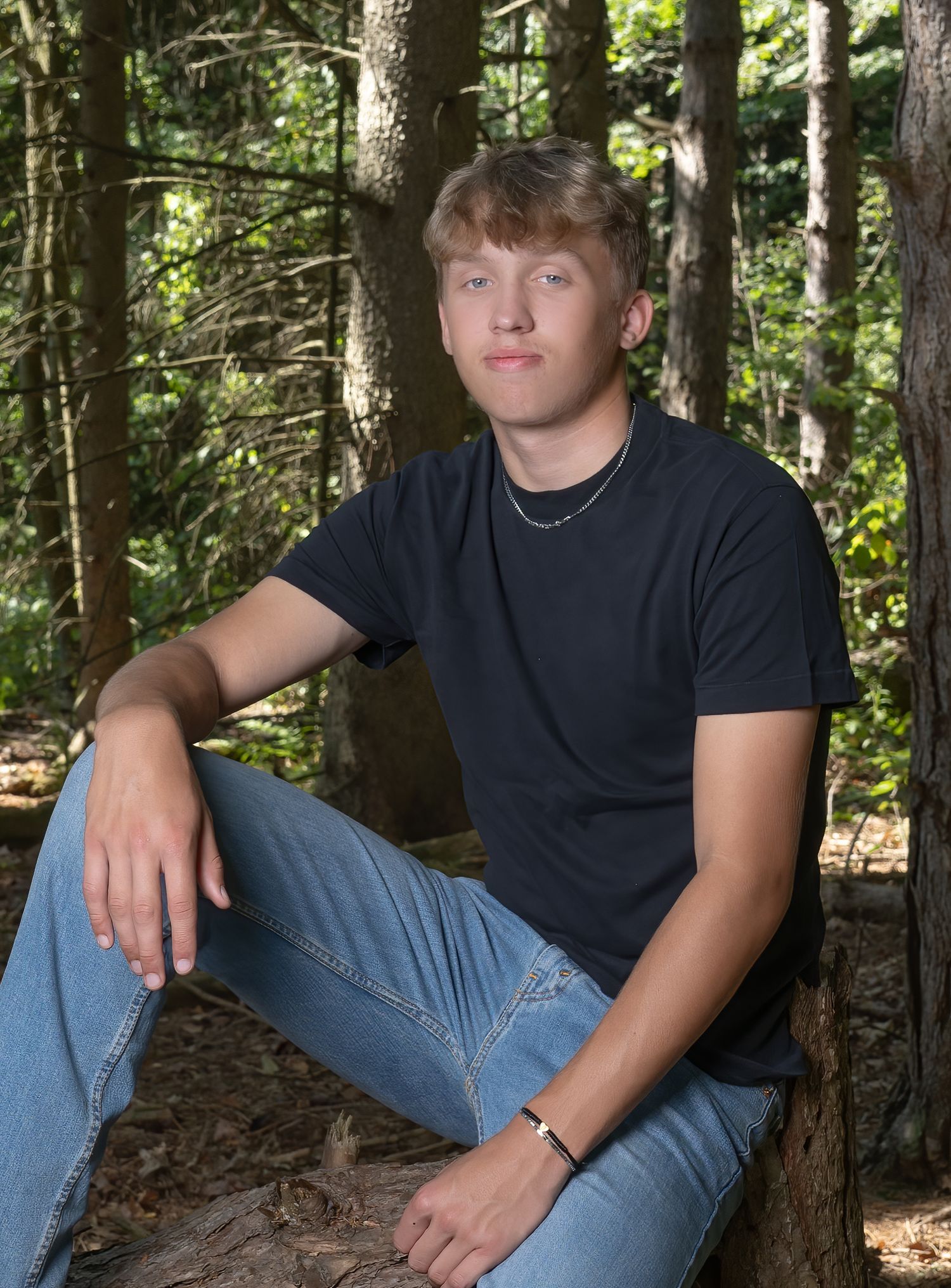 Casual outdoor portrait of person in black t-shirt sitting among trees.