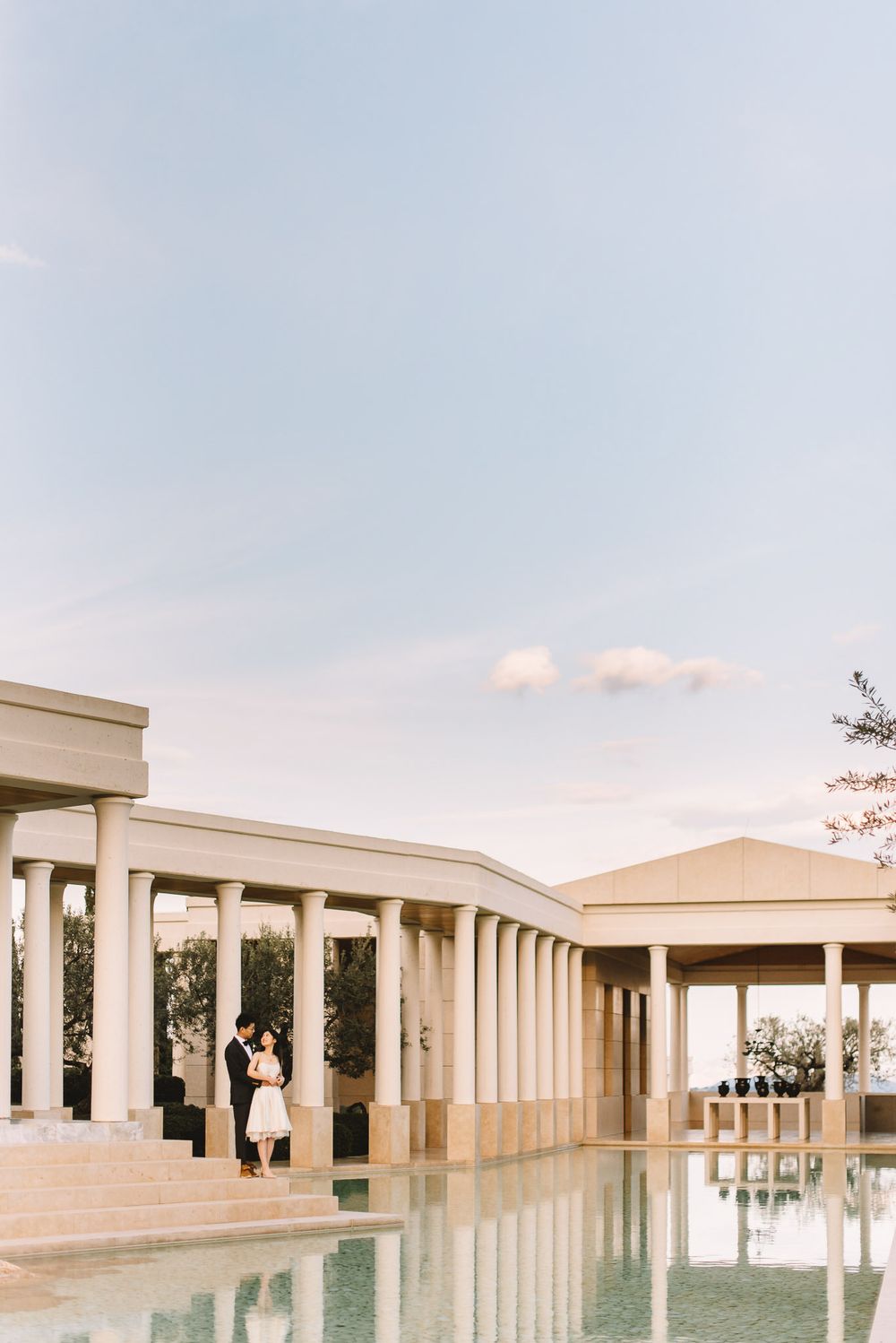 Couple standing by a reflective pool at a classical colonnade venue during golden hour.