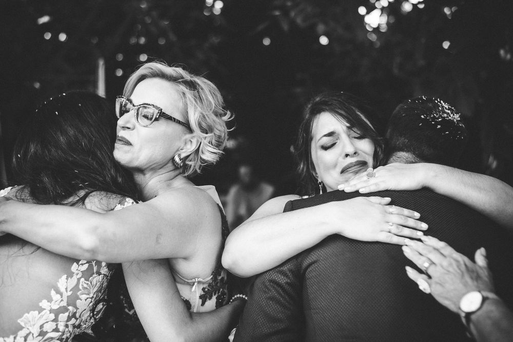 Black and white photo of a group of people sharing an emotional group hug at a wedding celebration.