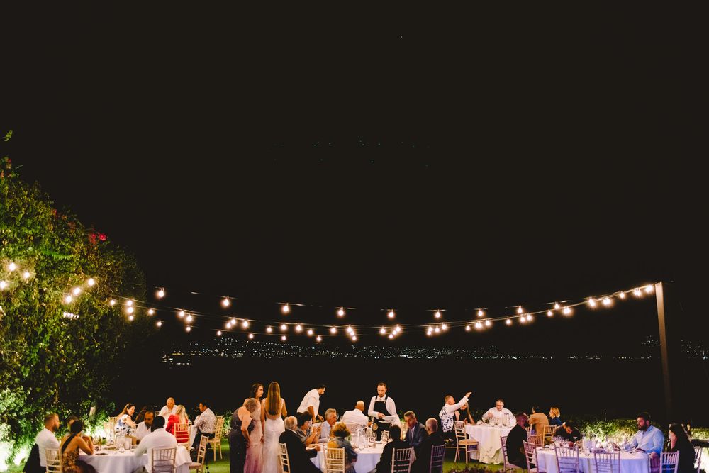 Outdoor evening wedding reception with string lights over guests dining al fresco against a dark night sky.