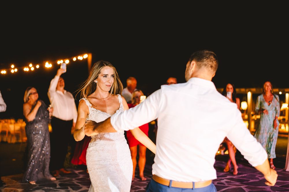 Bride and groom share first dance at outdoor wedding reception under string lights at night.