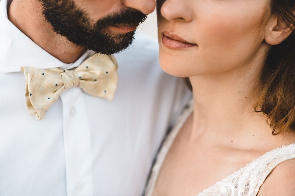 Close-up of a bride and groom in wedding attire, featuring a gold polka dot bow tie and lace bridal dress.