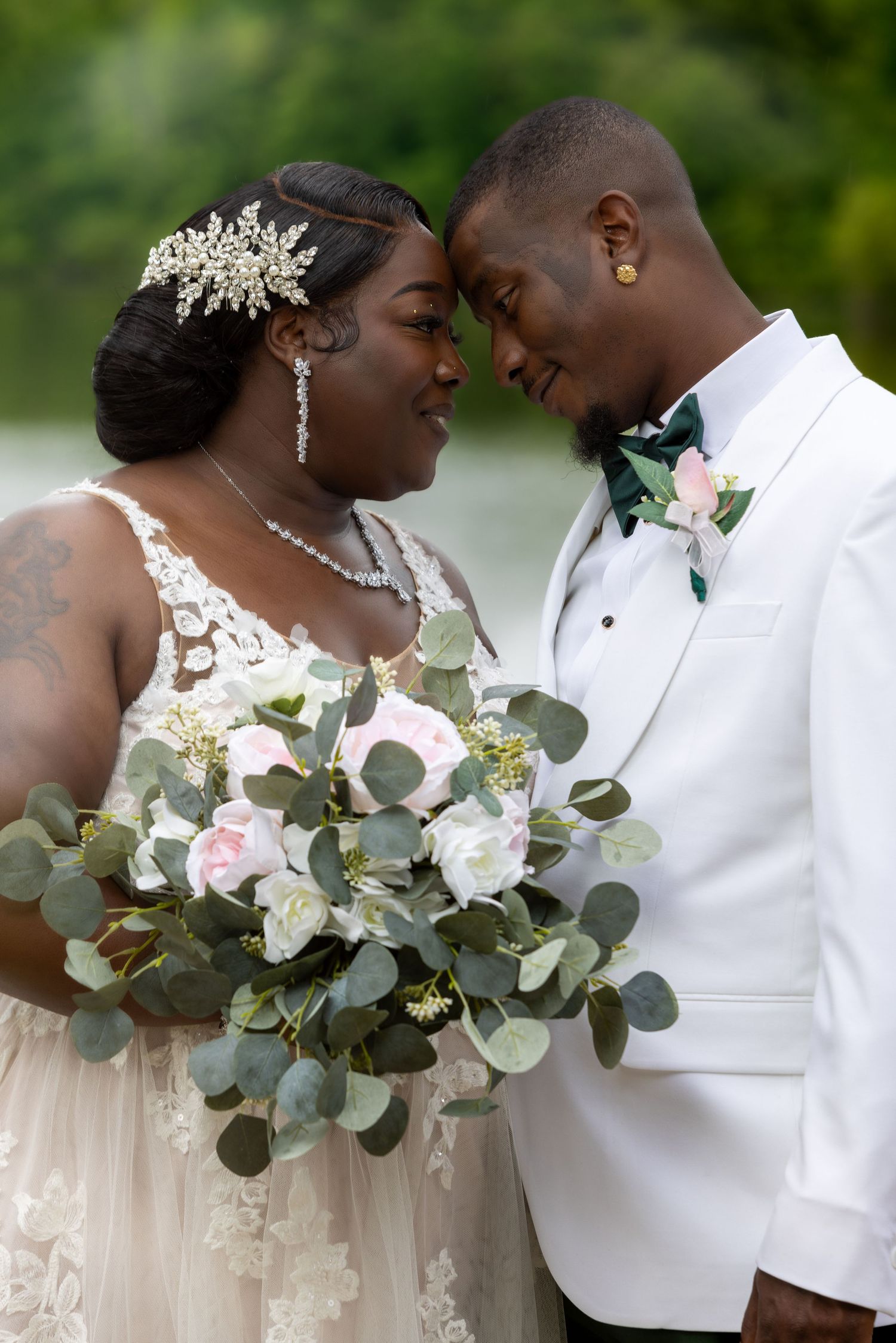 Romantic wedding couple shares intimate moment with eucalyptus and rose bouquet in outdoor setting.