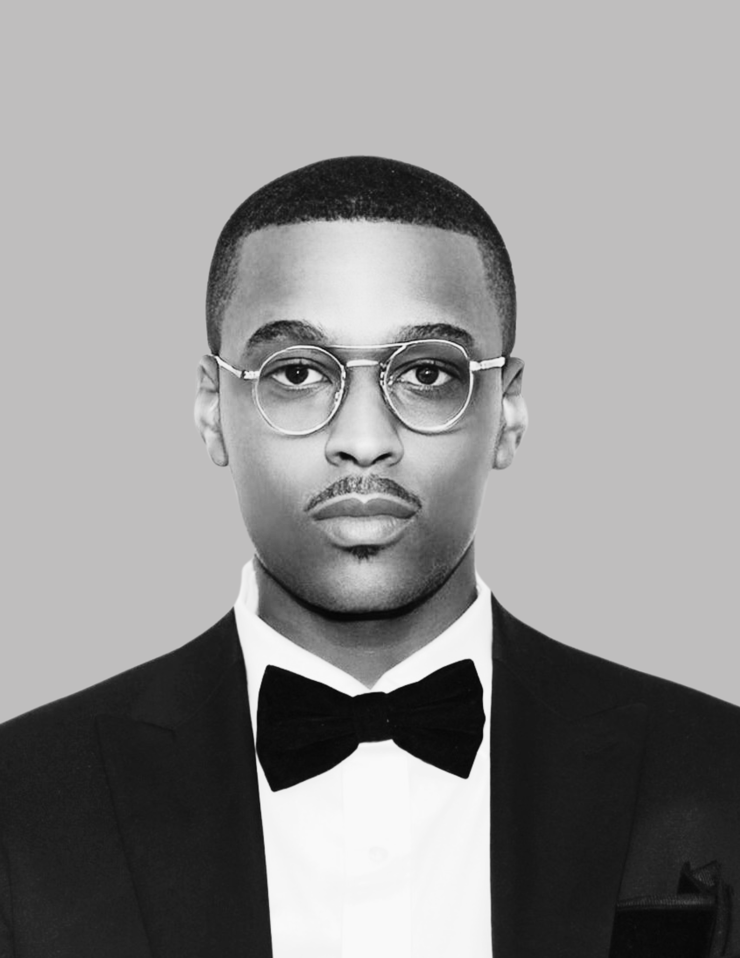 A portrait against a green background showing a person wearing glasses and a black bow tie with tuxedo.