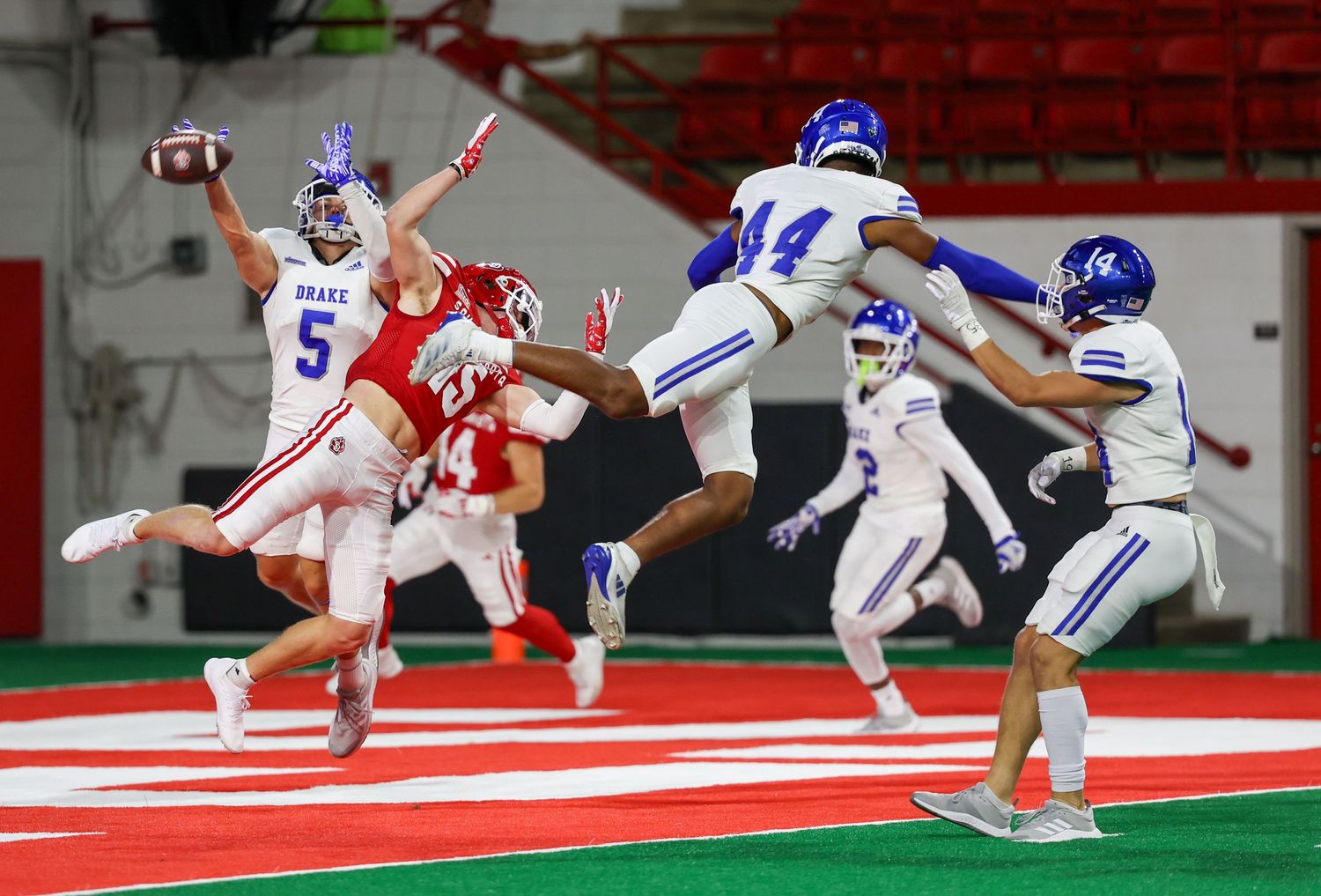The wide receiver over runs the pass in the endzone as many defenders also leap to try to catch the ball