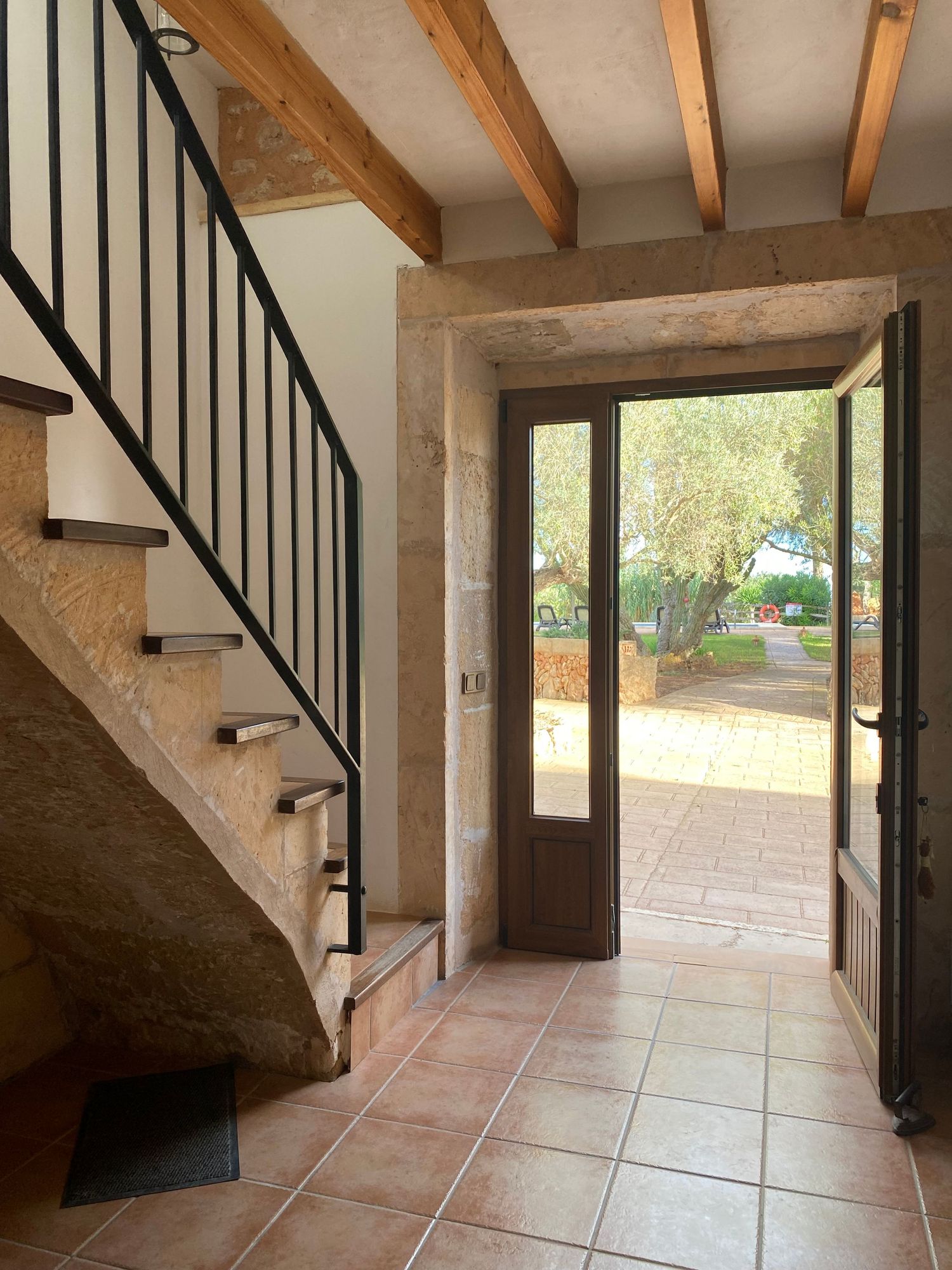 Stone entryway with curved staircase featuring iron railings and wooden beams overhead.