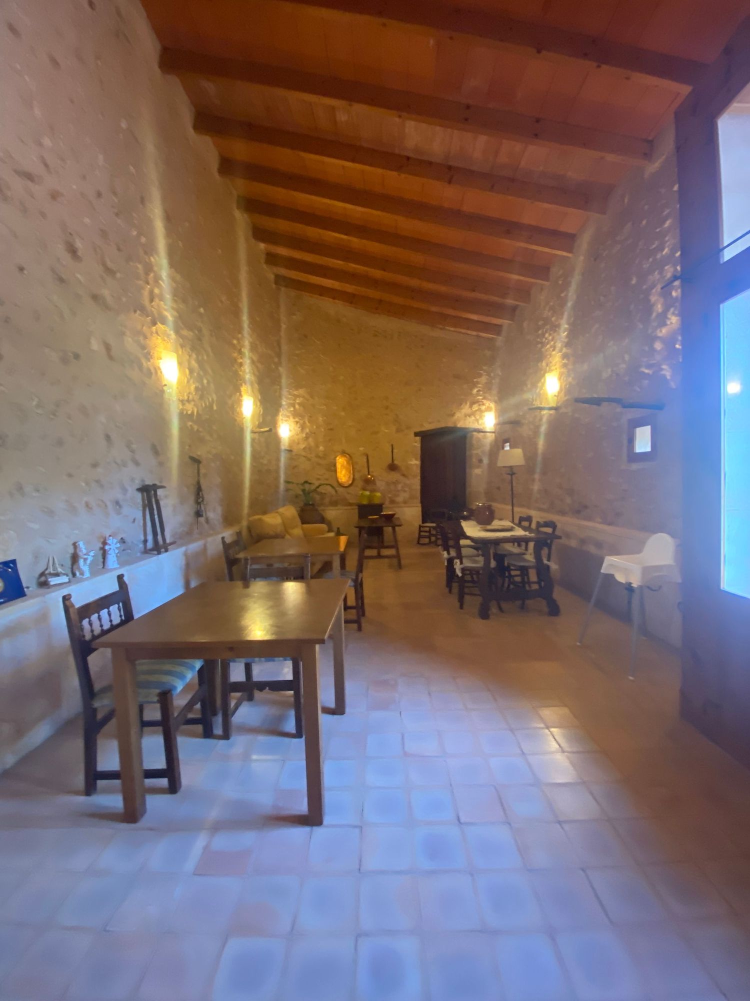 Long dining room with rustic stone walls, wooden beams, and terracotta flooring illuminated by pendant lights.