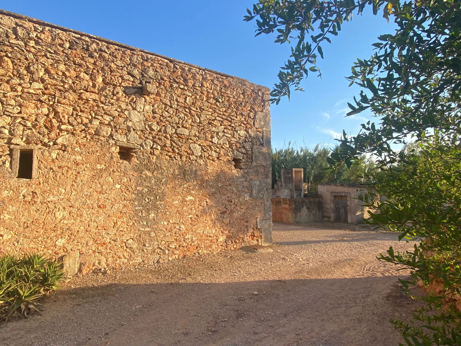 Historic stone wall structure with small windows along a dirt pathway.