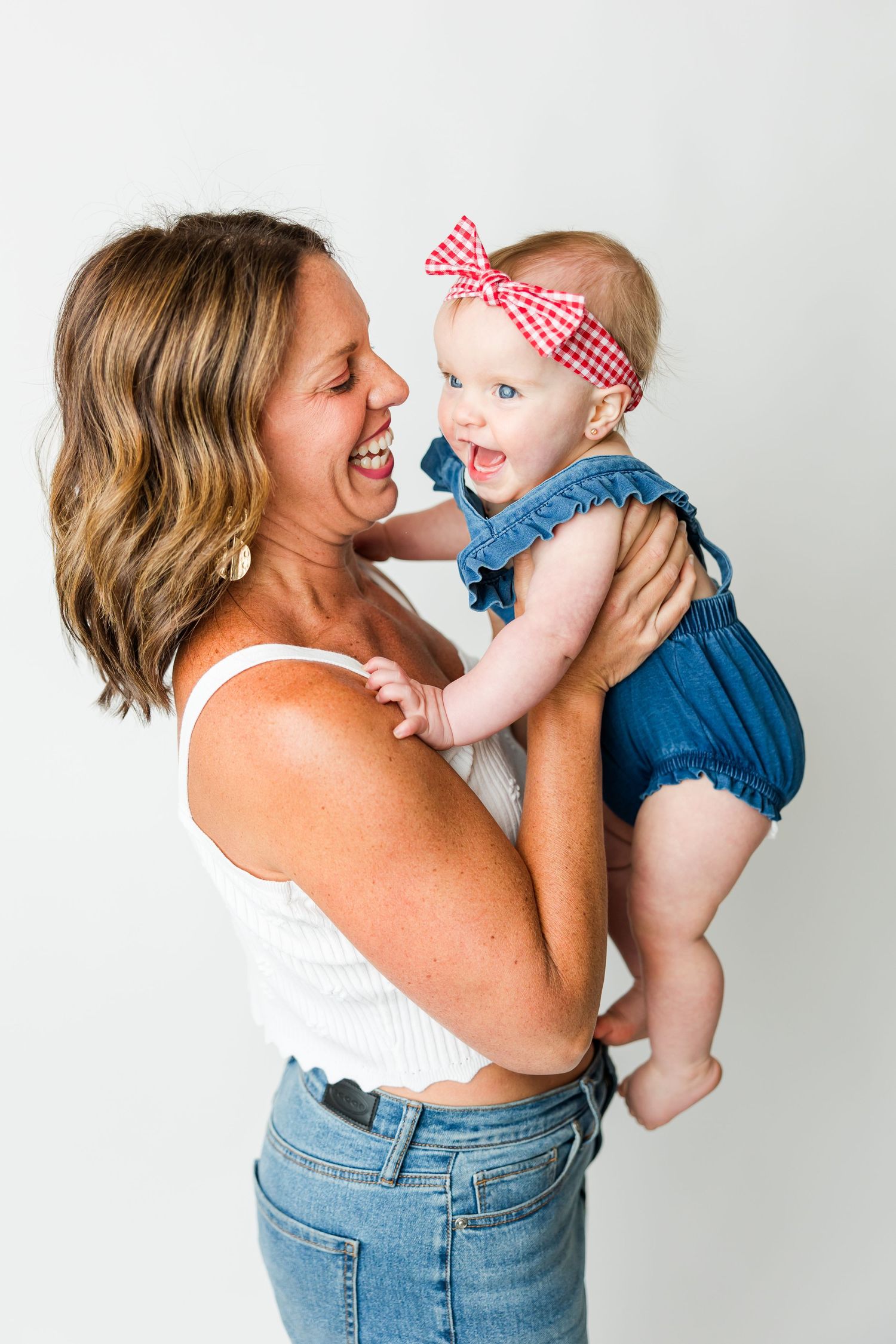 A joyful moment between parent and baby wearing a red checkered bow and blue romper against a white background.