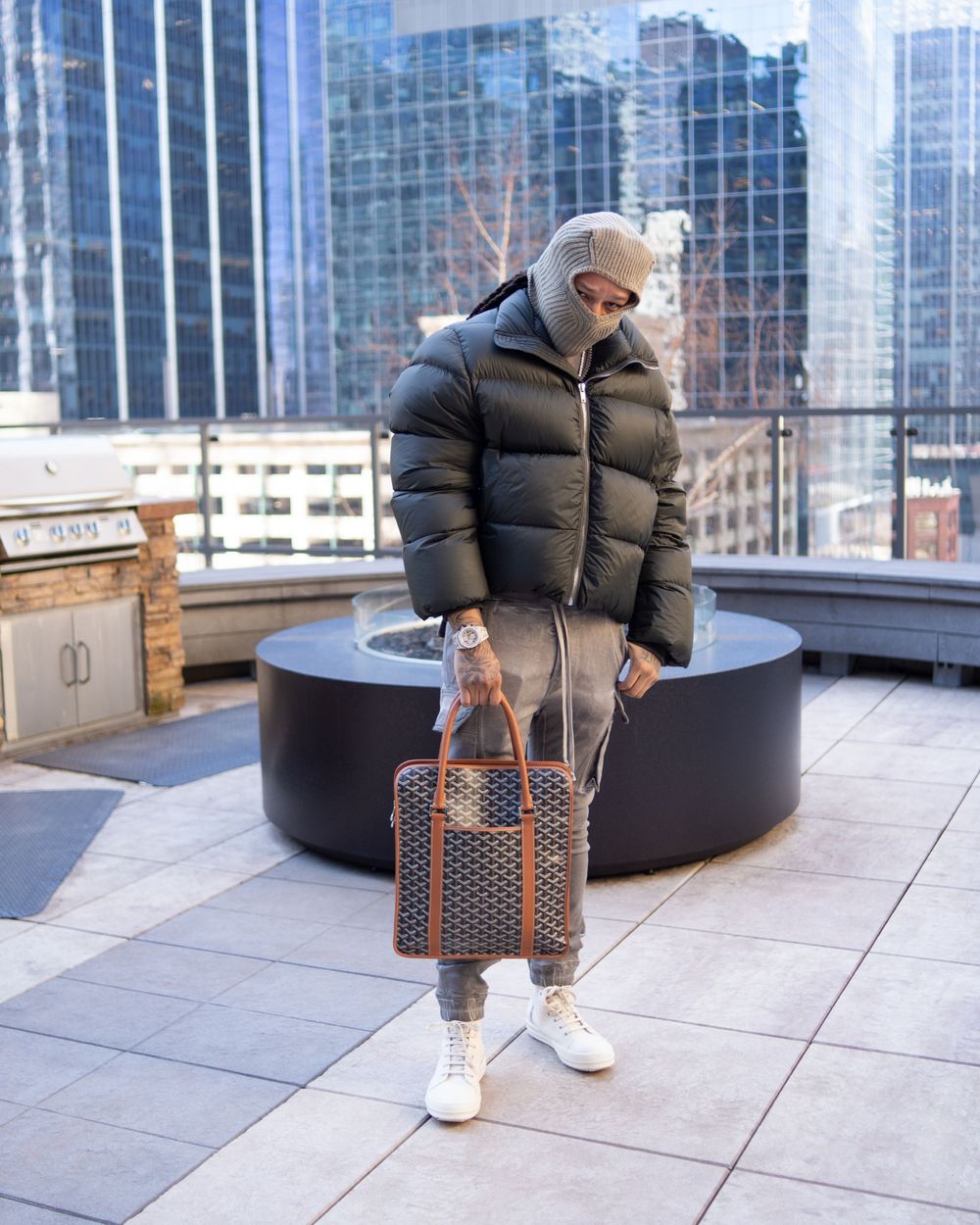 Urban fashion scene with person in winter coat and patterned duffle bag on modern rooftop.