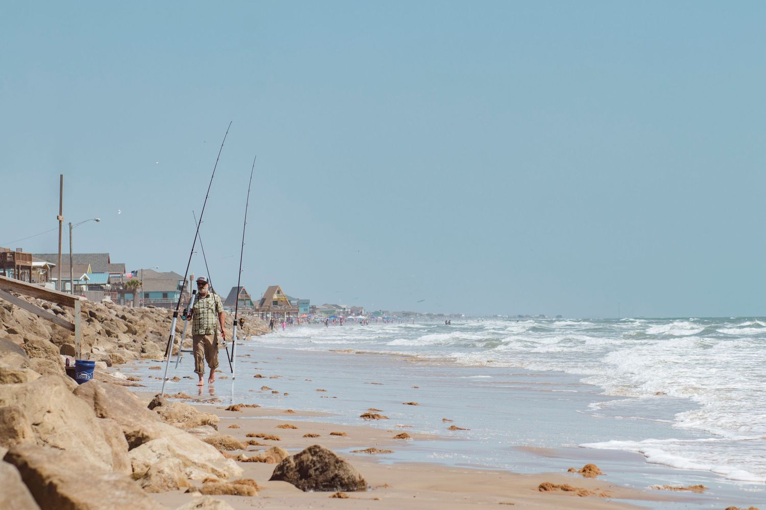 Fisherman in Surfside, Texas with 3 poles in the sand. the beach fades in the distance, with beach houses and waves. Freeport Surfside Texas