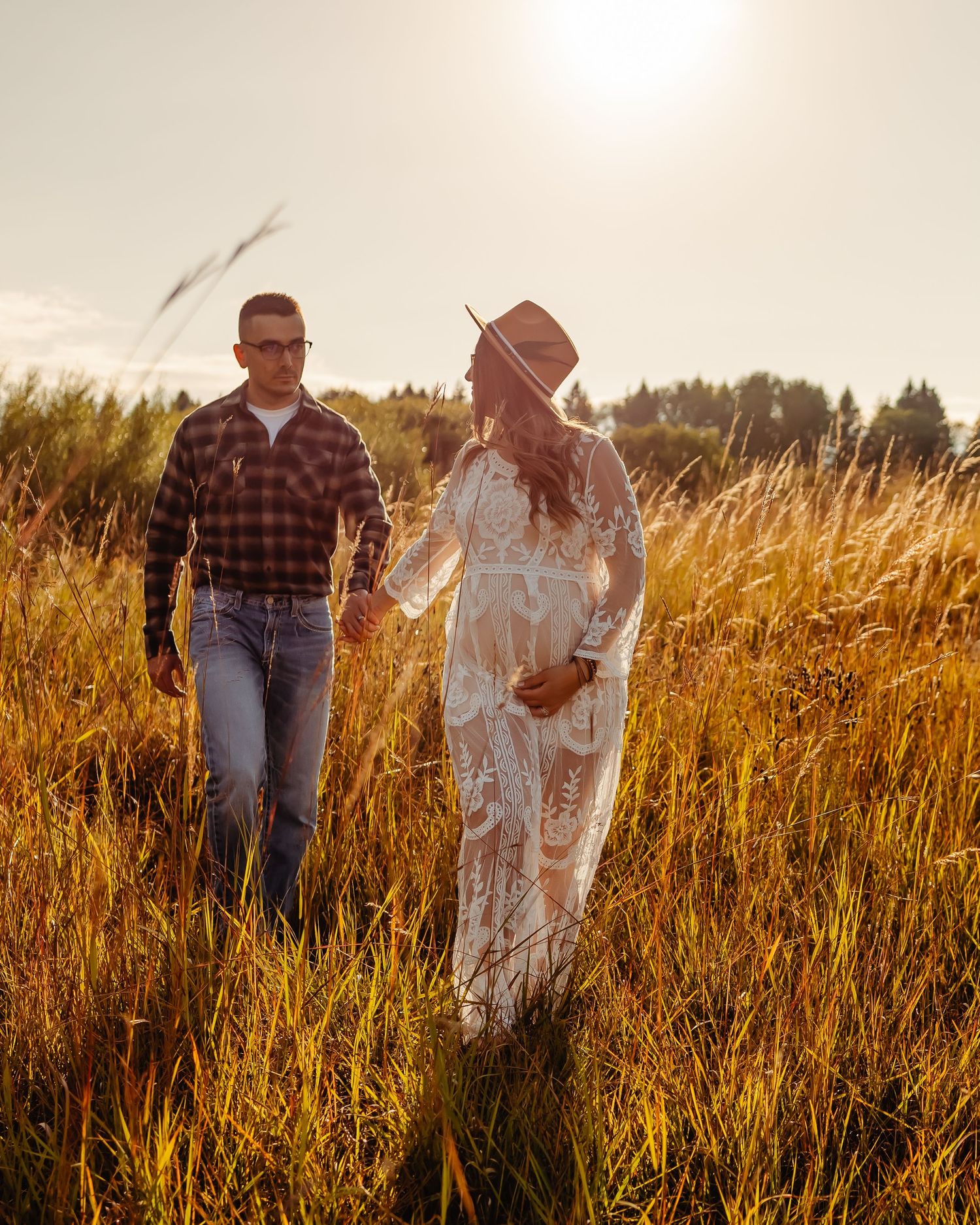 Two figures walk together through a golden wheat field at sunset, with light filtering through tall grass and trees in background.
