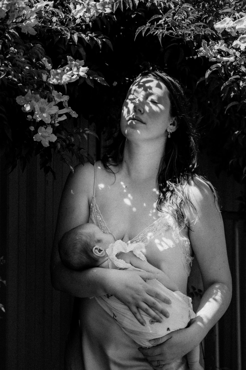 Black and white portrait of bonding moment with infant in natural lighting with leaf shadows.