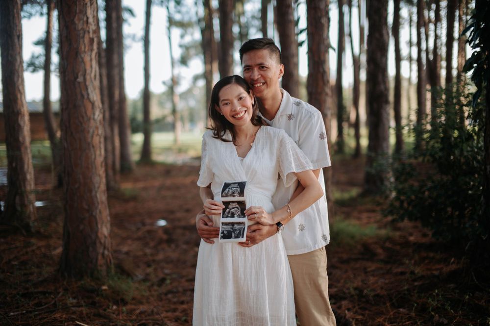 Couple holding ultrasound photos together in a pine forest during pregnancy announcement photoshoot.