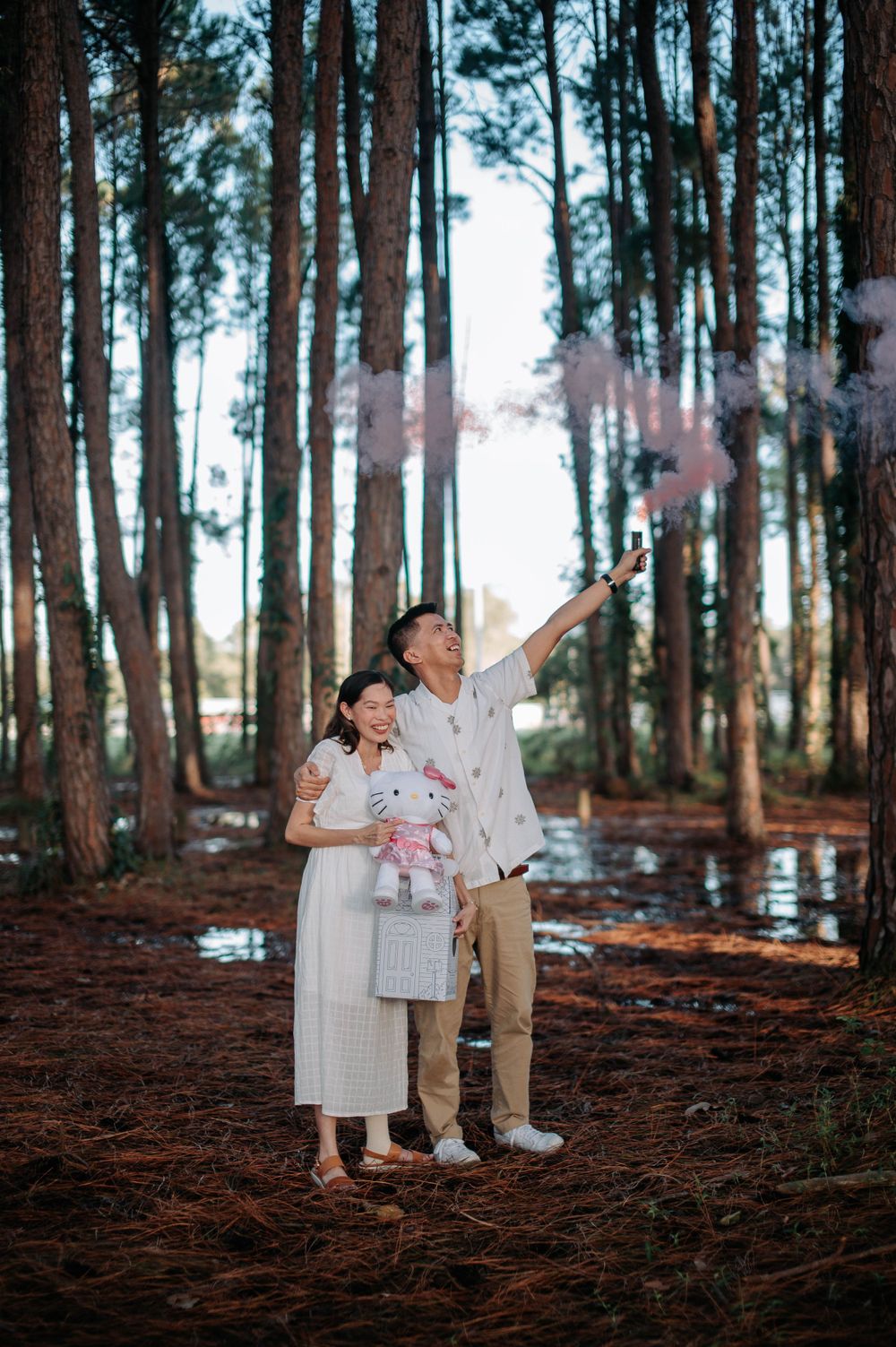 Couple with colorful smoke bombs enjoying a playful moment in a forest setting.