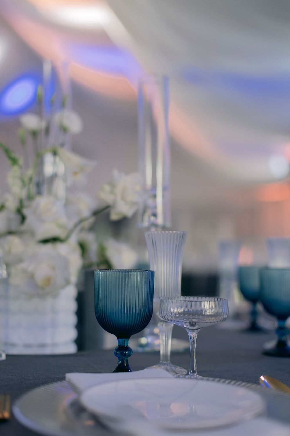 Blue ribbed goblet and crystal glassware on an elegant wedding reception table setting.