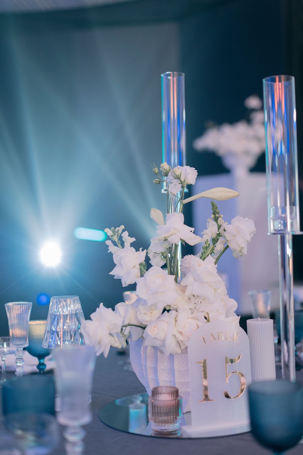 White floral centerpiece with tall glass cylinders and table number 15 at an elegant wedding reception.