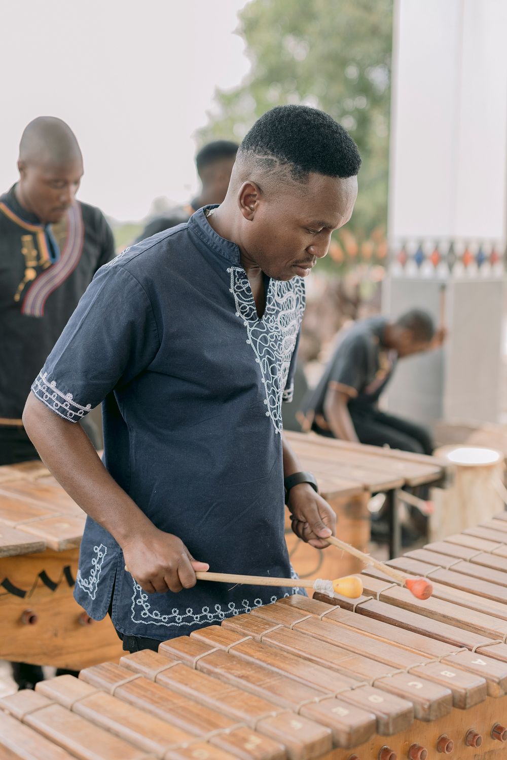 A musician plays a wooden xylophone marimba instrument at an outdoor cultural event in Africa.
