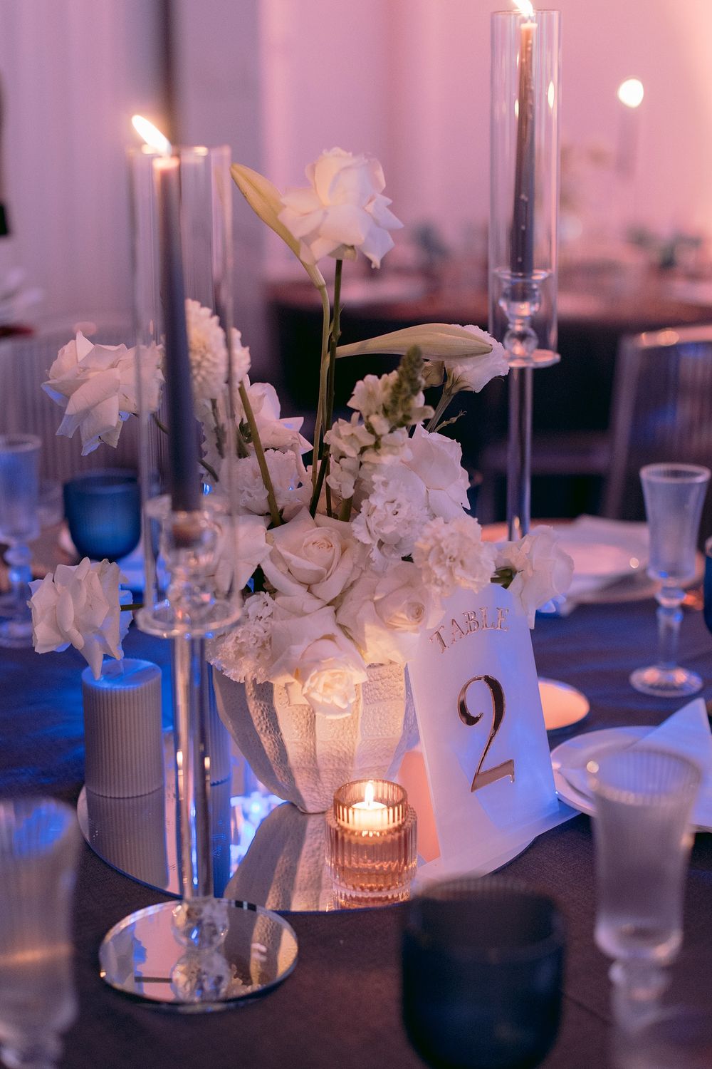 White floral centerpiece with roses and candles on table number 2 at an elegant wedding reception.