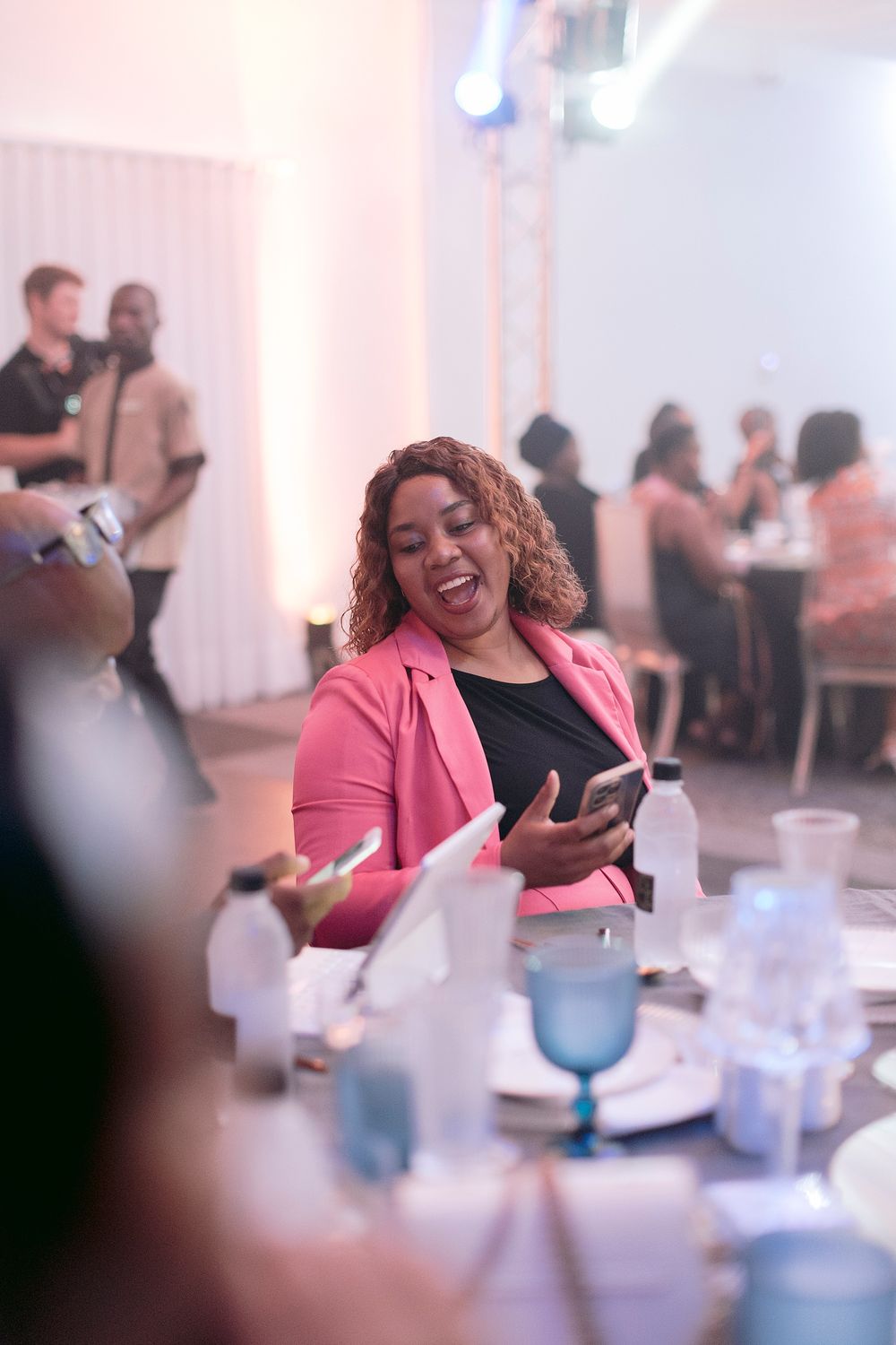 Smiling woman in pink blazer using smartphone at elegant event dinner table.