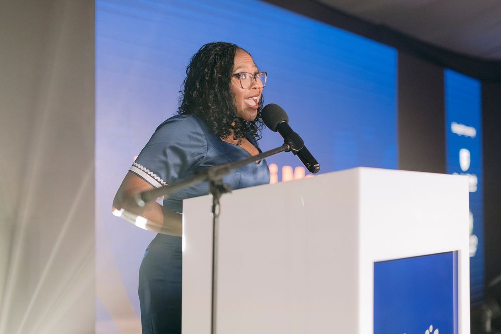 Woman speaking at white podium during formal conference event.