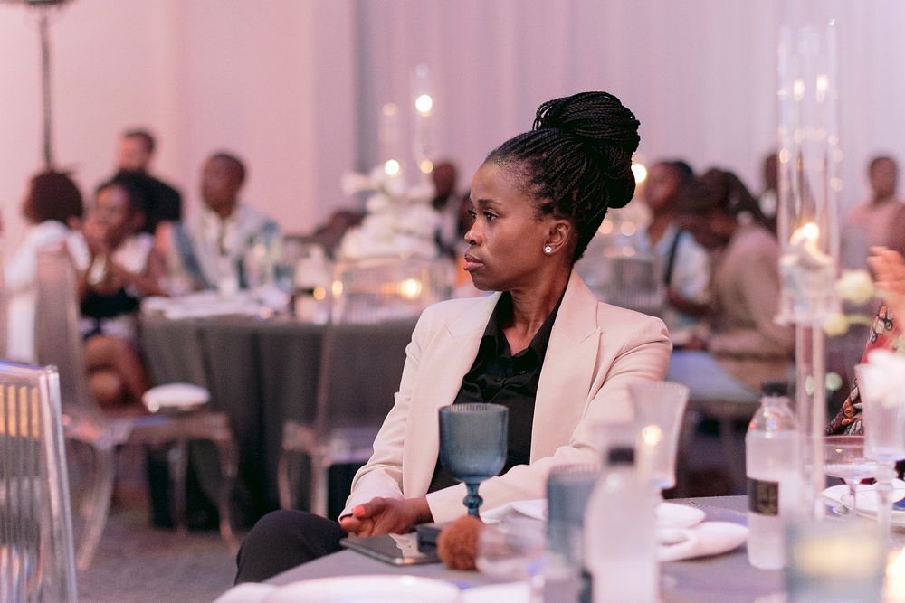 Woman in white blazer seated attentively at candlelit formal banquet event.