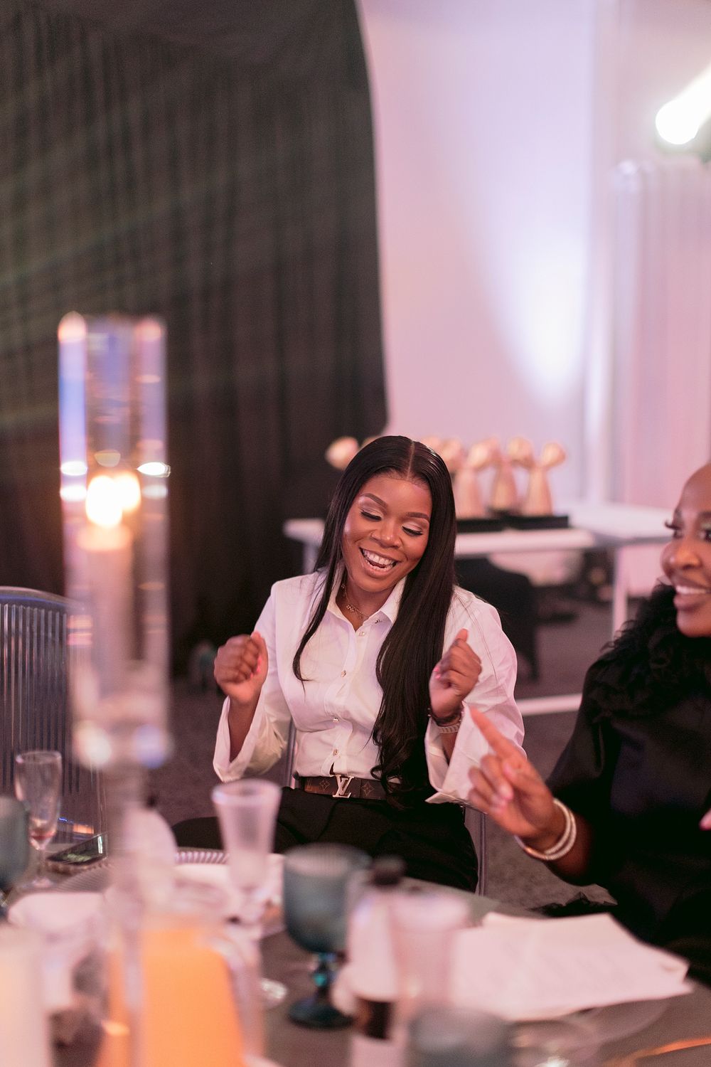A joyful woman in a white blazer laughs and dances at an elegant gala dinner event.