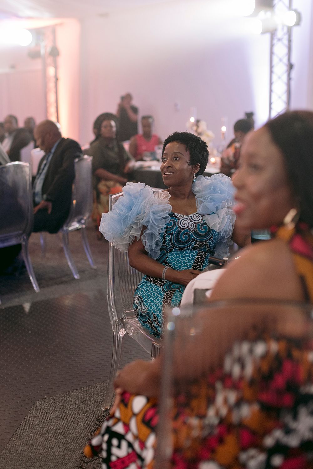 A woman in a vibrant blue African print dress with ruffled sleeves smiles at a gala event.