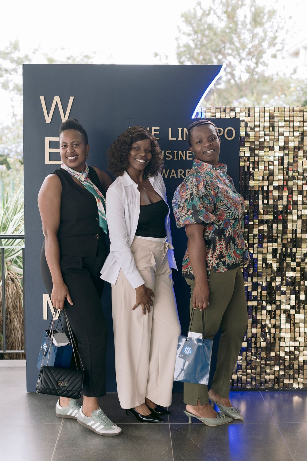 Three women posing together at the Limpopo Business Awards event in front of a decorative gold mosaic backdrop.