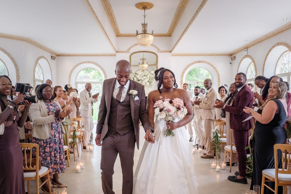 Joyful newlyweds celebrate while walking down the aisle at an elegant wedding ceremony with guests cheering.