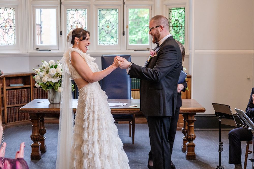 Bride and groom exchanging rings during wedding ceremony in elegant chapel with stained glass windows.