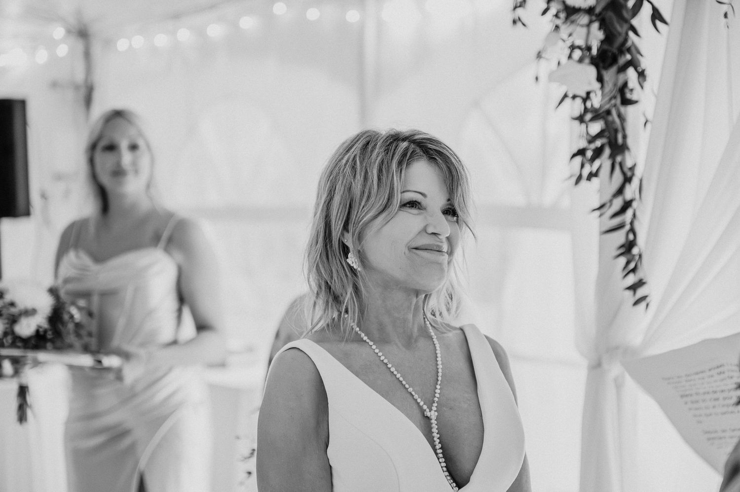 Bride in elegant white dress stands under twinkling lights during wedding reception.