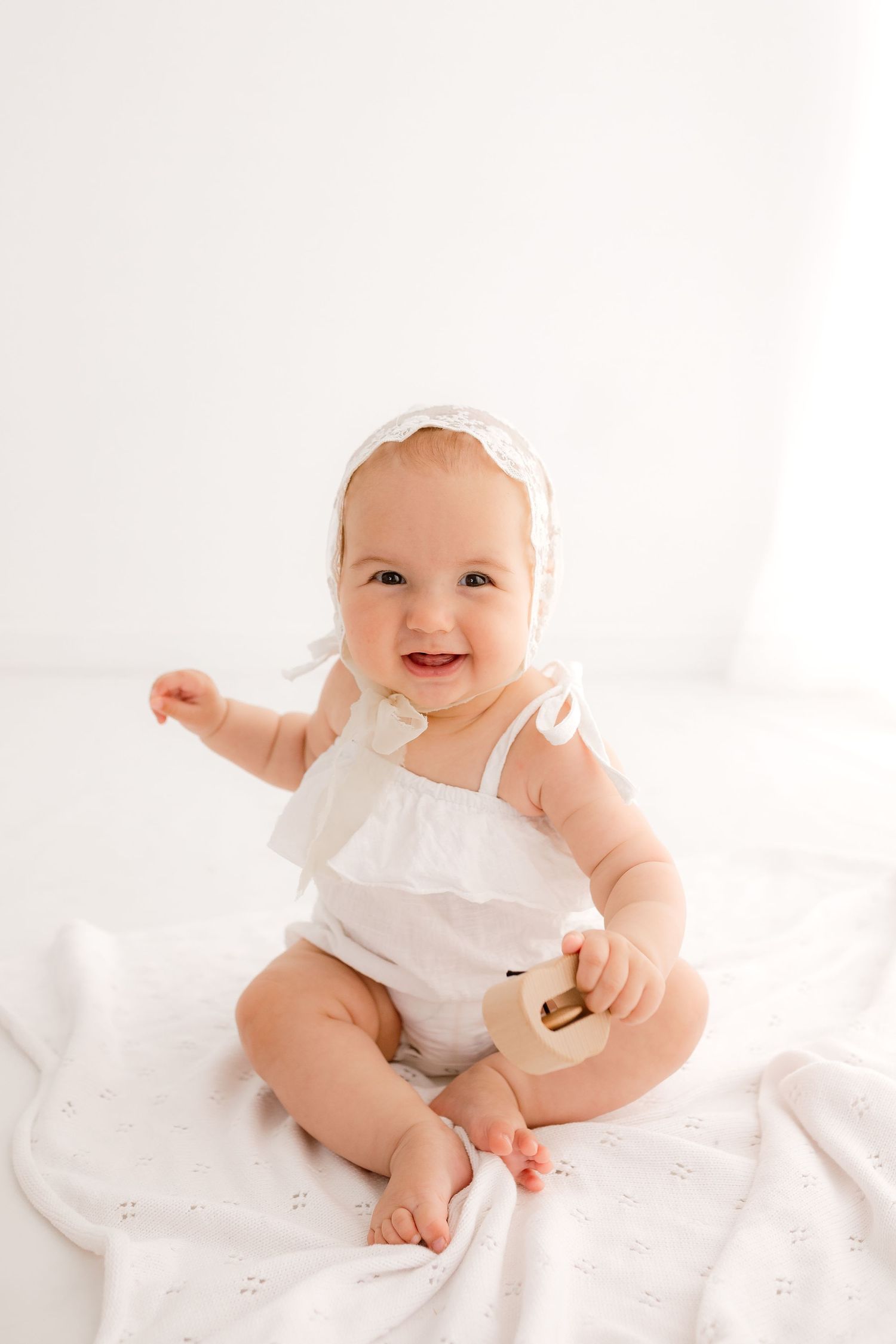 Happy baby in white romper sitting and playing during studio photo session.