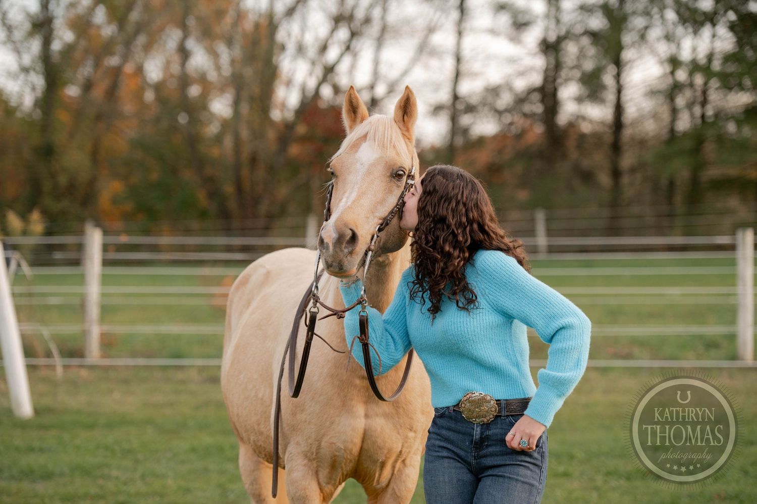 Close-up of palomino horse with rider in blue sweater against autumn background.