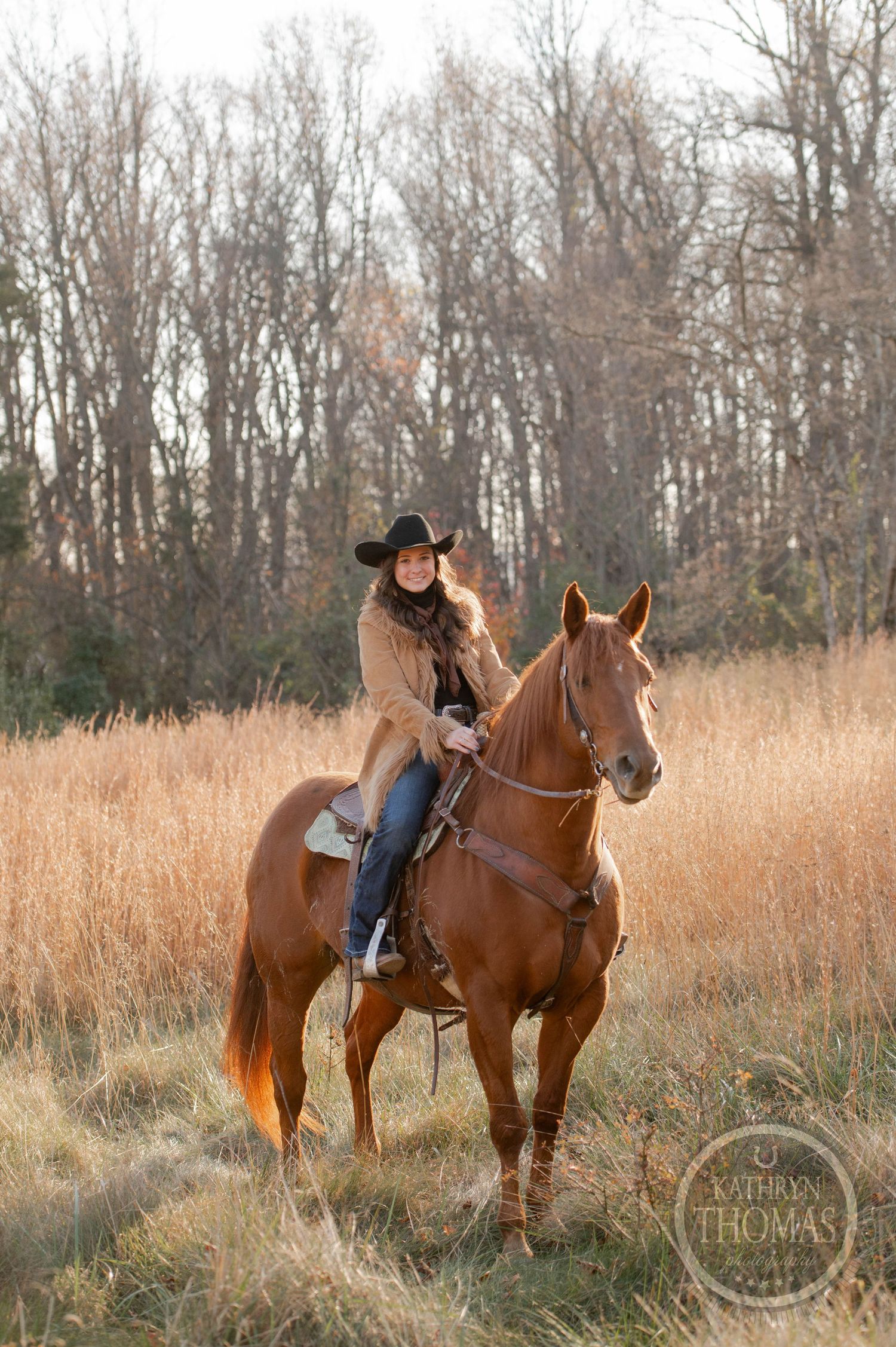A western rider in cowboy hat guides a chestnut horse through golden autumn grass.