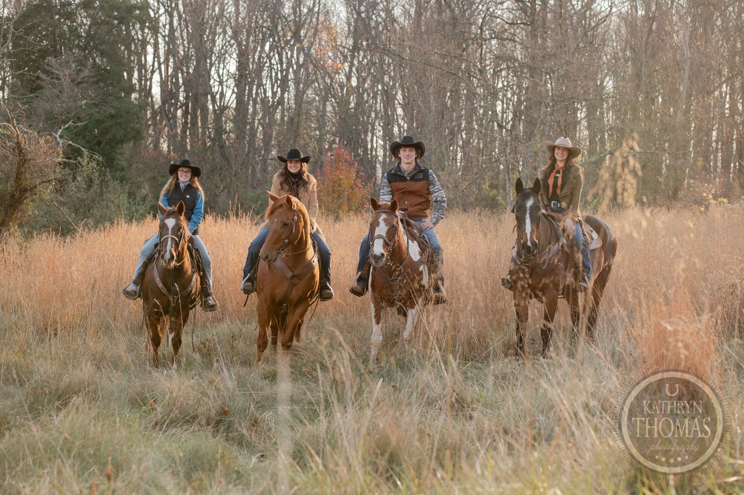 Group of riders on horseback galloping through tall brown grass in late autumn.