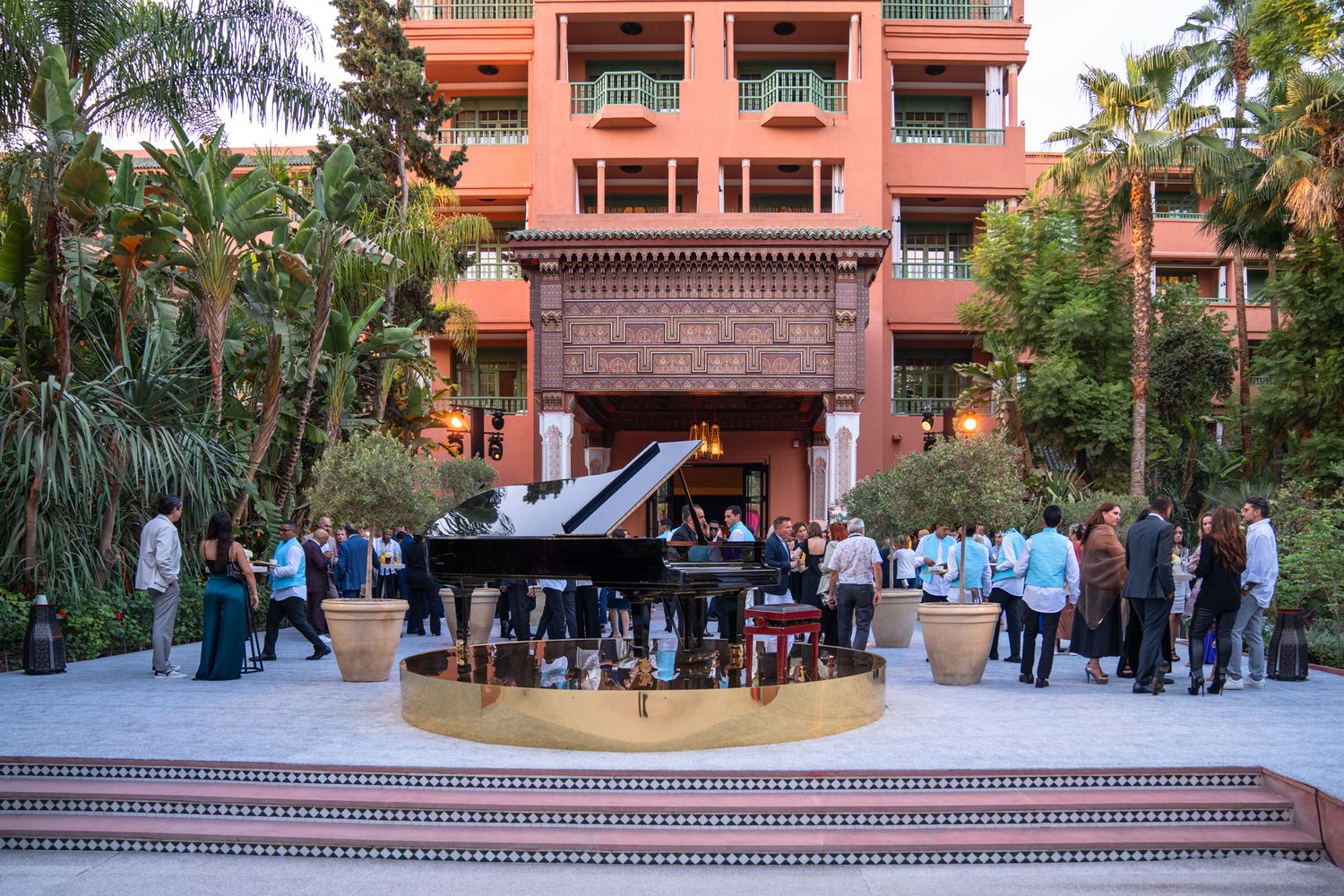 An outdoor piano performance takes place on a terrace at a Mediterranean-style resort with coral-colored architecture.