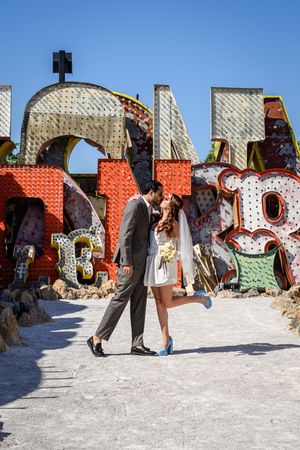 Newlywed couple sharing a romantic kiss at the Neon Museum in Las Vegas, surrounded by colorful vintage signs.