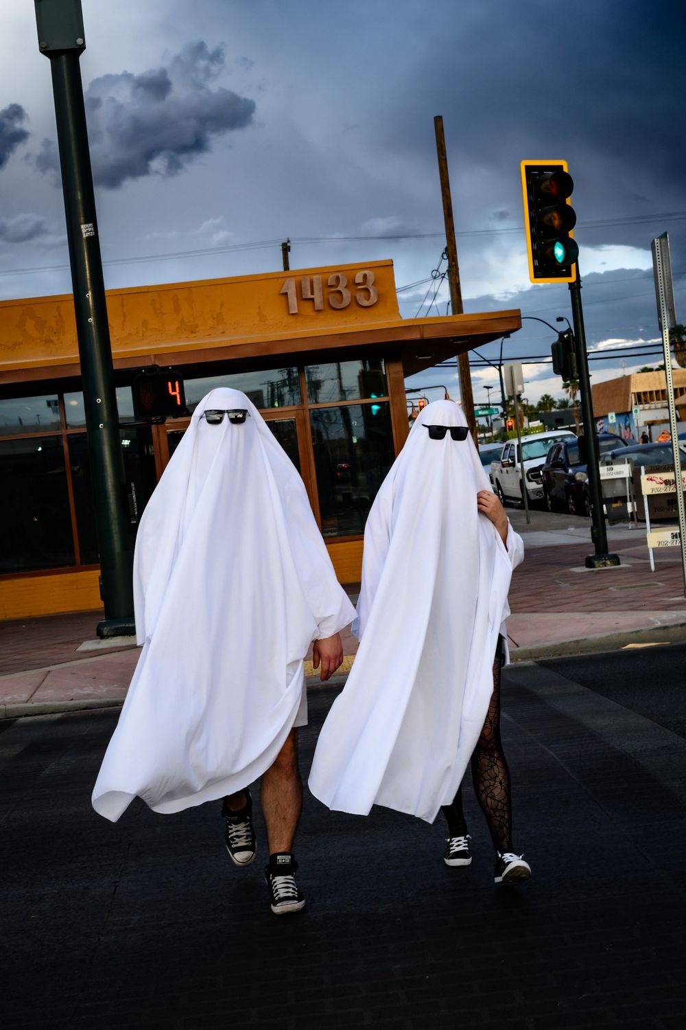 Two figures in ghost costumes walk past a storefront under dramatic cloudy skies.